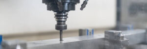 A drill held by a chuck in a vertical position drilling a hole in a metal block
